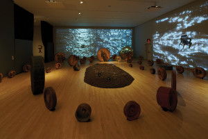 Whitfield Lovell (b. 1959); Deep River, 2013; 56 wood discs, found objects, soil, video projections and sound; size variable; Courtesy of the artist and DC Moore Gallery, New York.